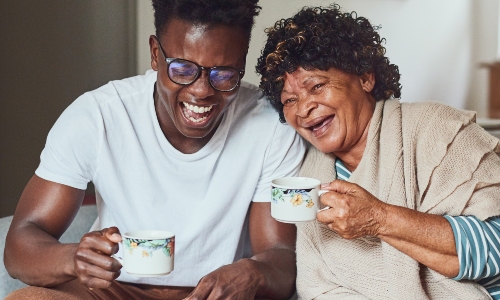 A young man laughs with his grandmother while drinking tea