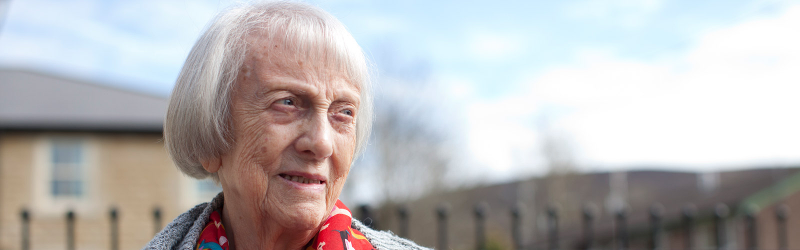 An older woman wearing a red scarf looks into the distance