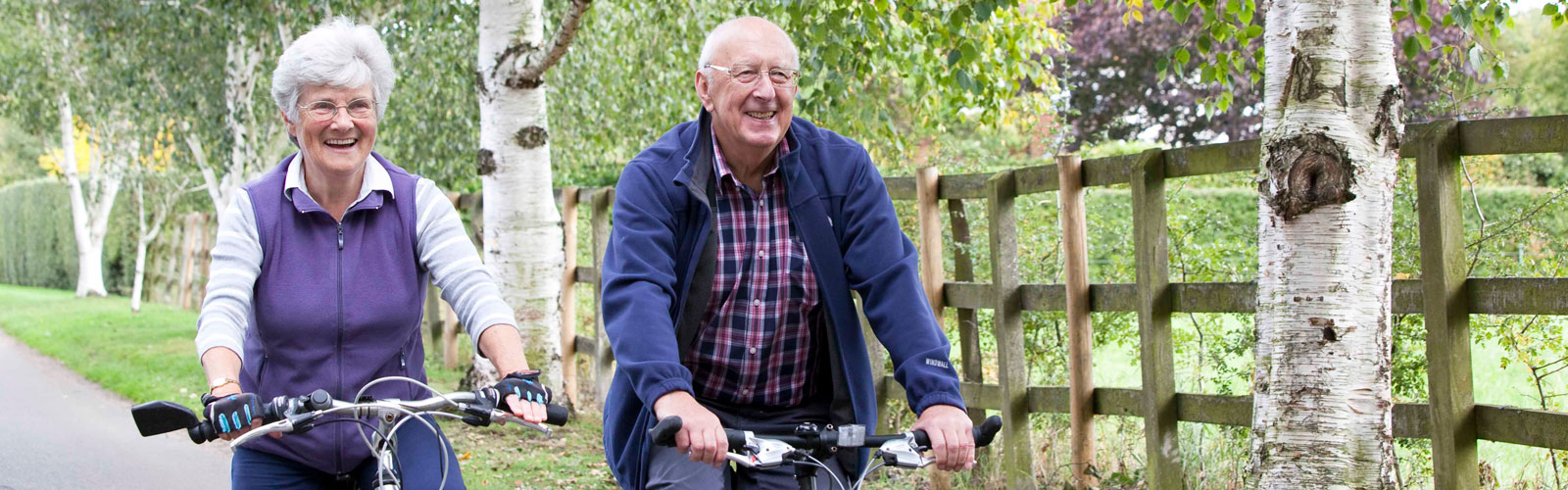 An older couple, a man and a woman, riding bikes next to one another.