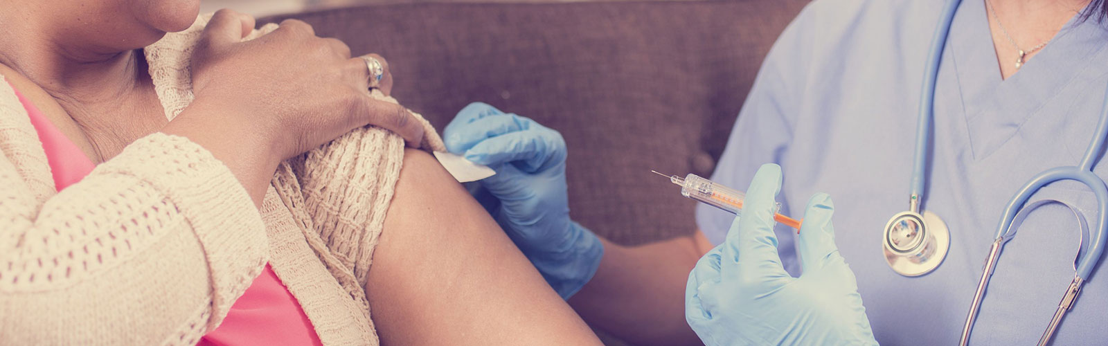 A woman in blue gives an injection to an older woman