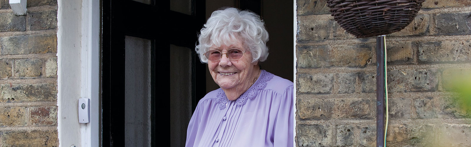 An older woman, looking out of the front door of her house