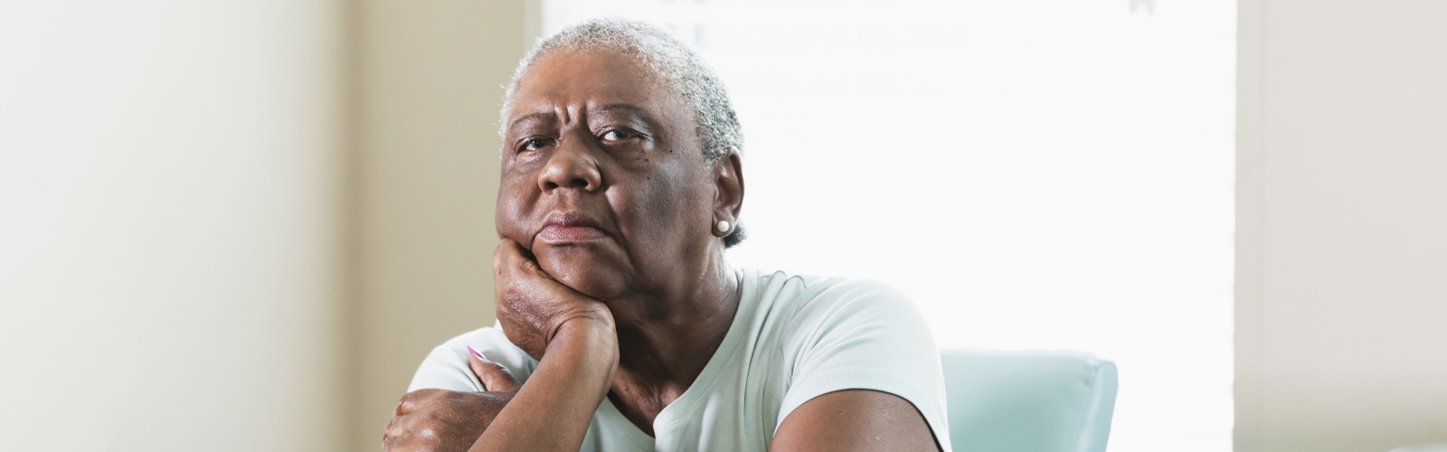 An older lady, with her chin resting on her hand, sits at a table