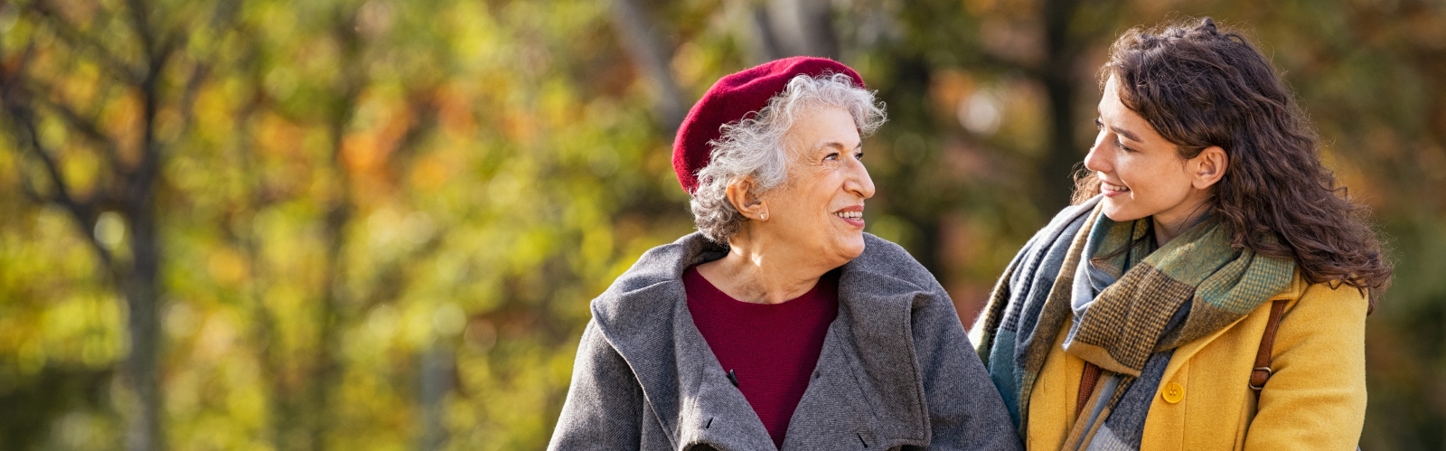 An older woman and a younger woman walking through a park arm-in-arm