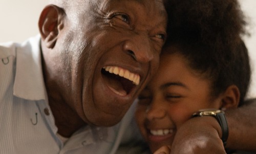 A Black older man laughing and hugging his granddaughter 