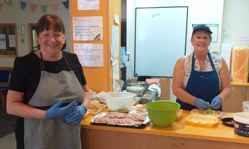 Two ladies, both wearing blue protective gloves, stand in a kitchen