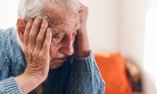 An older man looks sad with his head in his hands