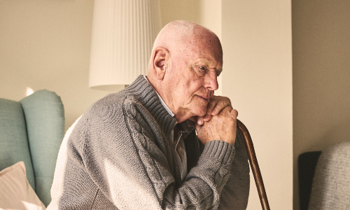 Older man with walking stick looks sadly into the distance