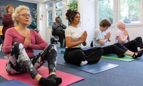 A group of women sit cross-legged on mats practising yoga