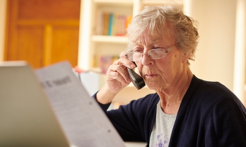 An older lady on the phone, looking concerned at her bill