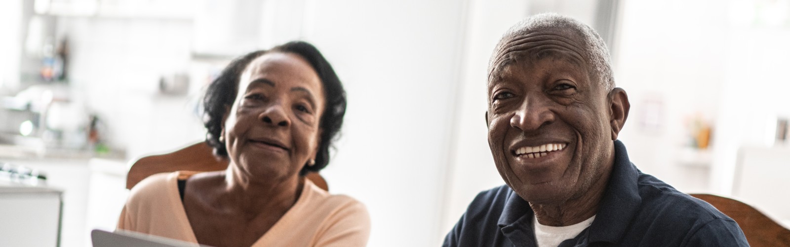 A Black older woman and Black older man sit together, looking towards the camera, smiling