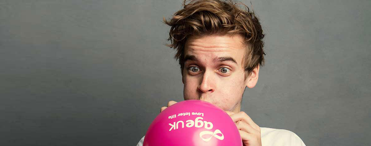 Joe Sugg, Age UK Ambassador, blowing up a balloon